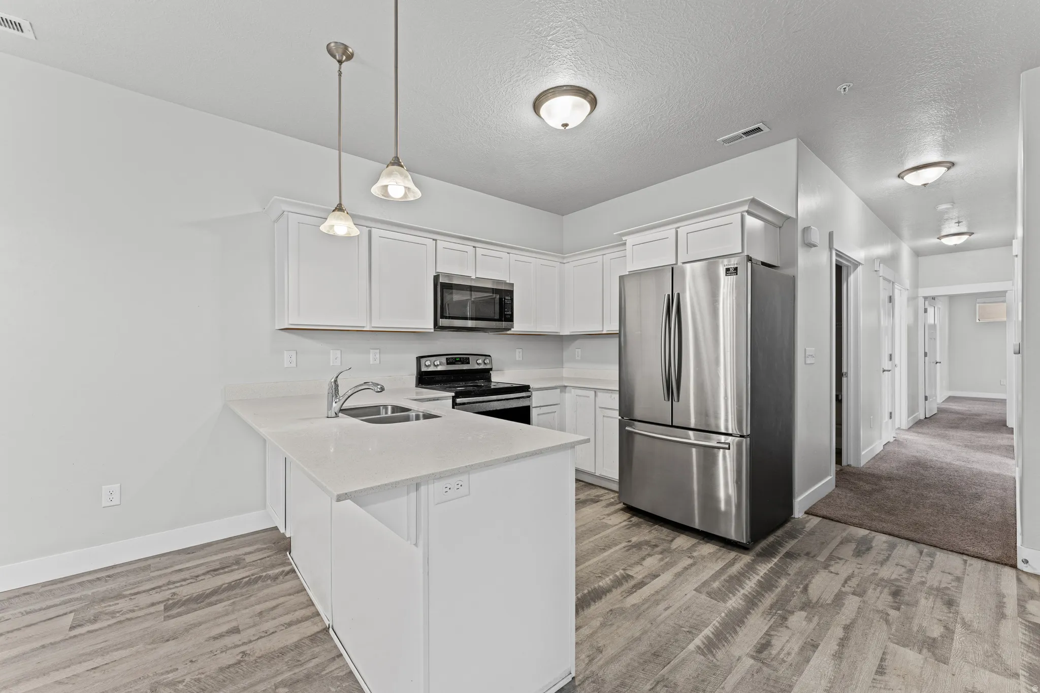 Kitchen featuring stainless steel appliances, white cabinetry, a peninsula, pendant lighting, and light stone countertops