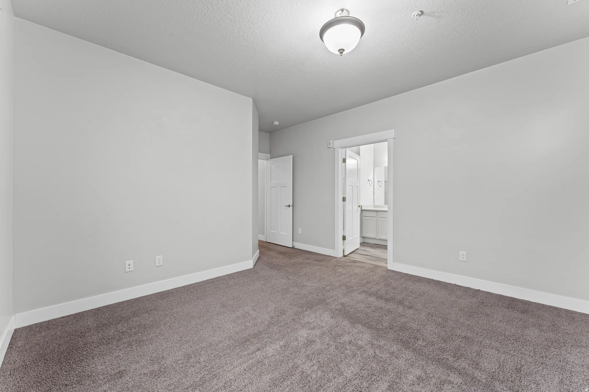 Unfurnished bedroom with carpet flooring, ensuite bath, and a textured ceiling