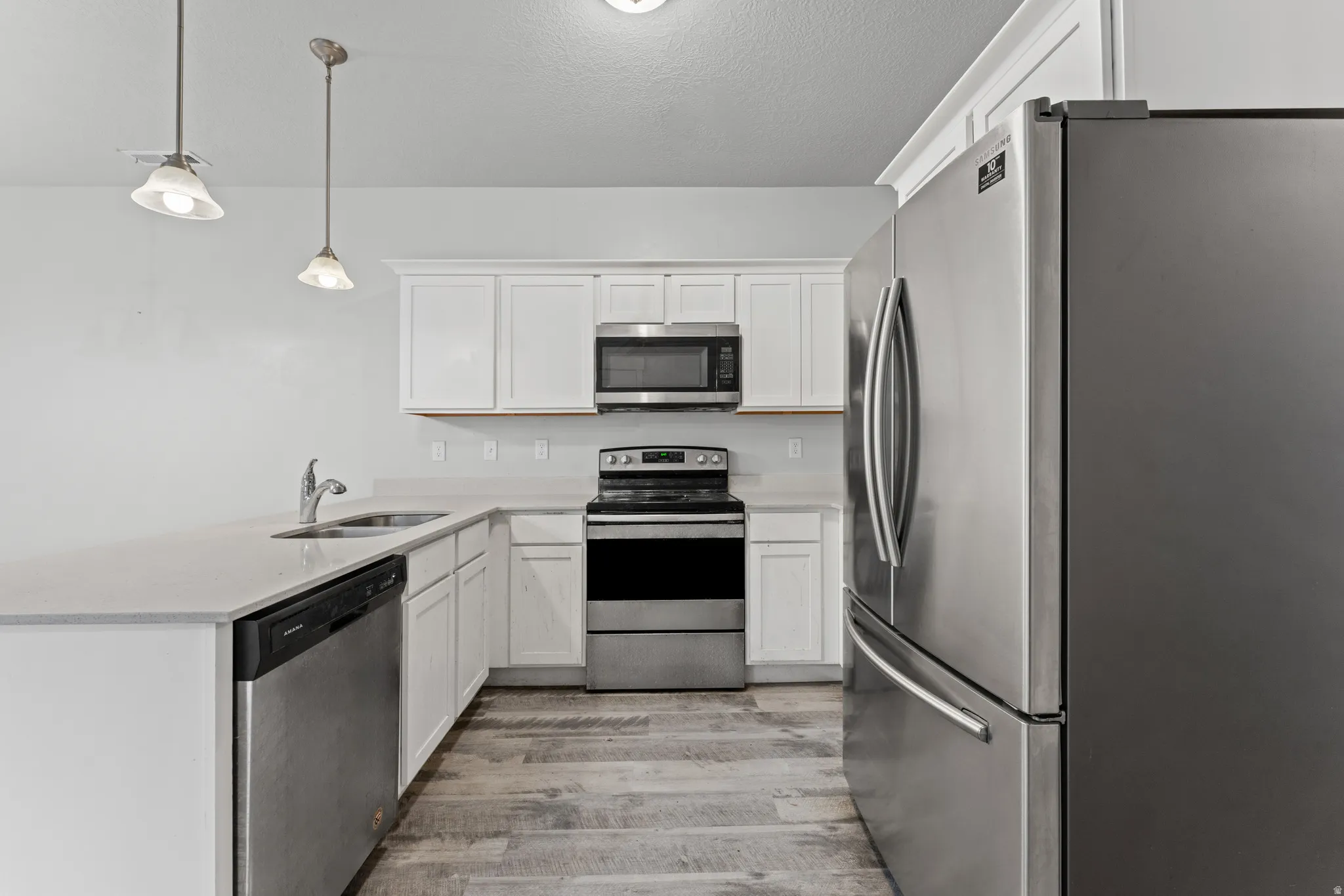 Kitchen featuring stainless steel appliances, a peninsula, decorative light fixtures, white cabinets, and a textured ceiling