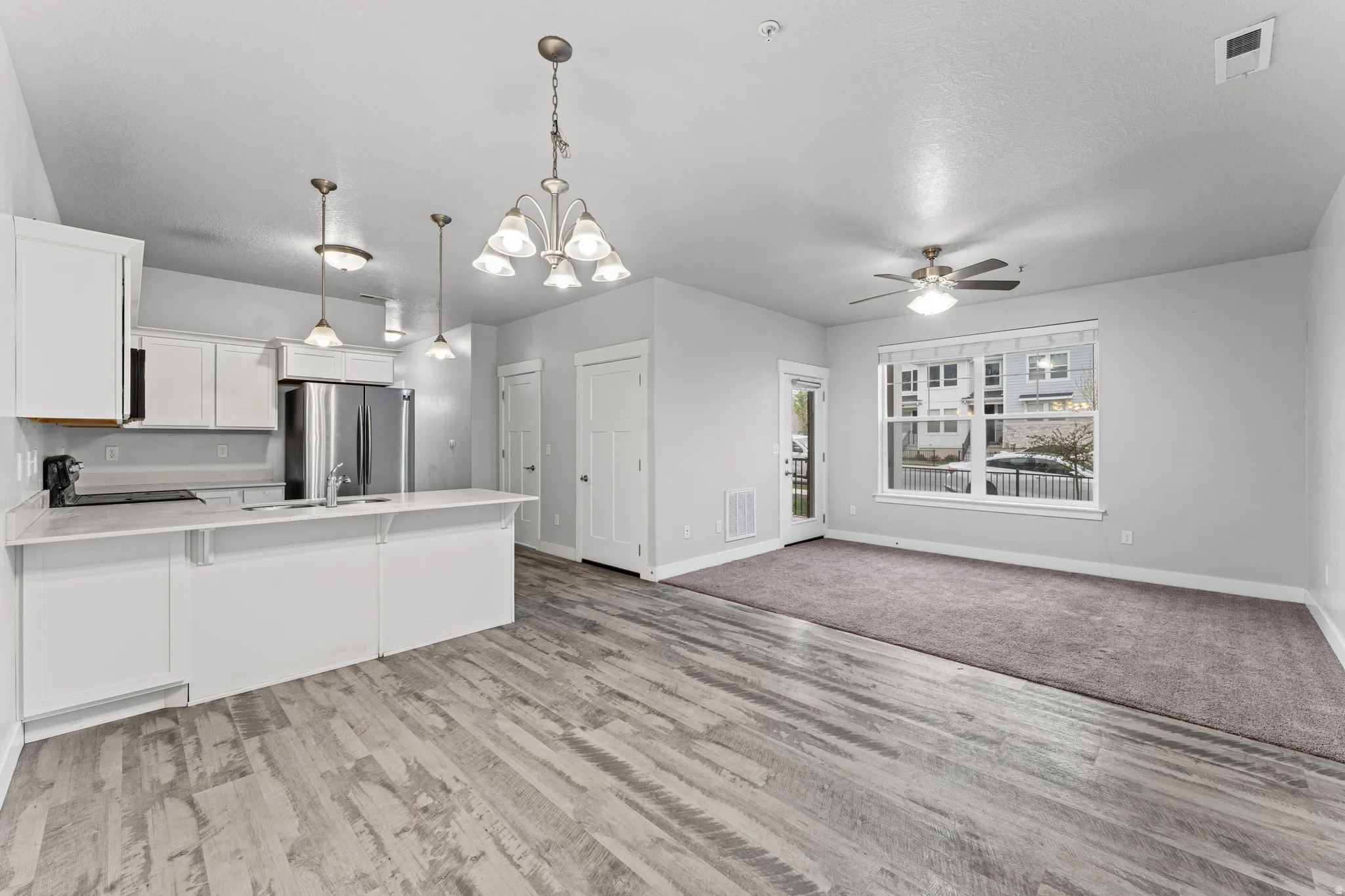 Kitchen with open floor plan, white cabinetry, hanging lights, a peninsula, and freestanding refrigerator
