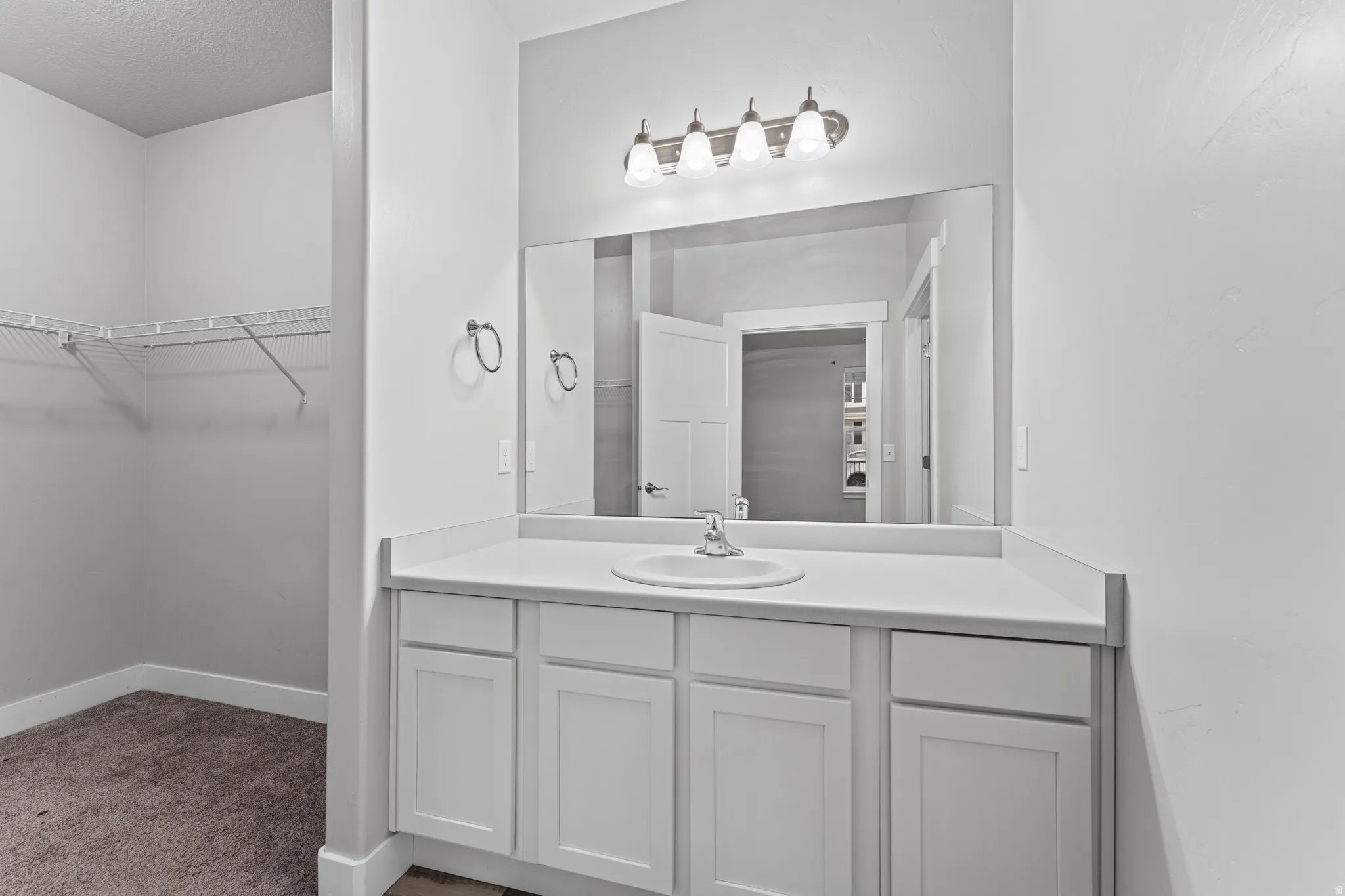 Bathroom with vanity, a walk in closet, carpet floors, and a textured ceiling