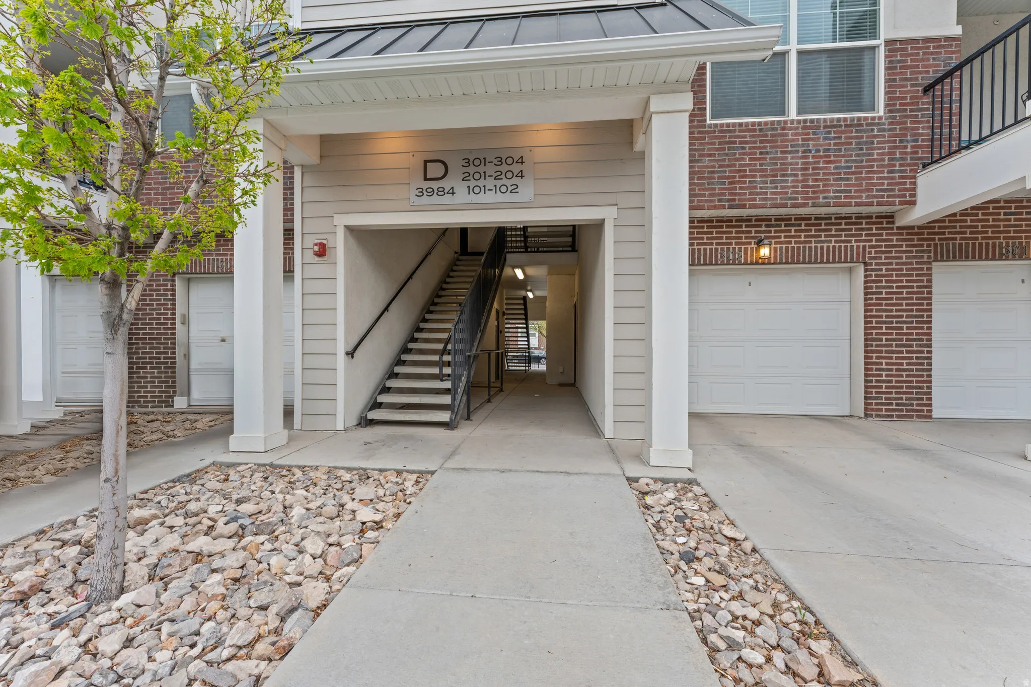 Property entrance with a standing seam roof, driveway, a garage, and brick siding
