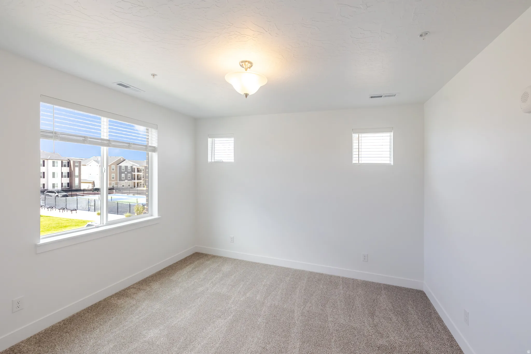 Carpeted room with multiple windows, a ceiling-mounted light fixture, and white walls