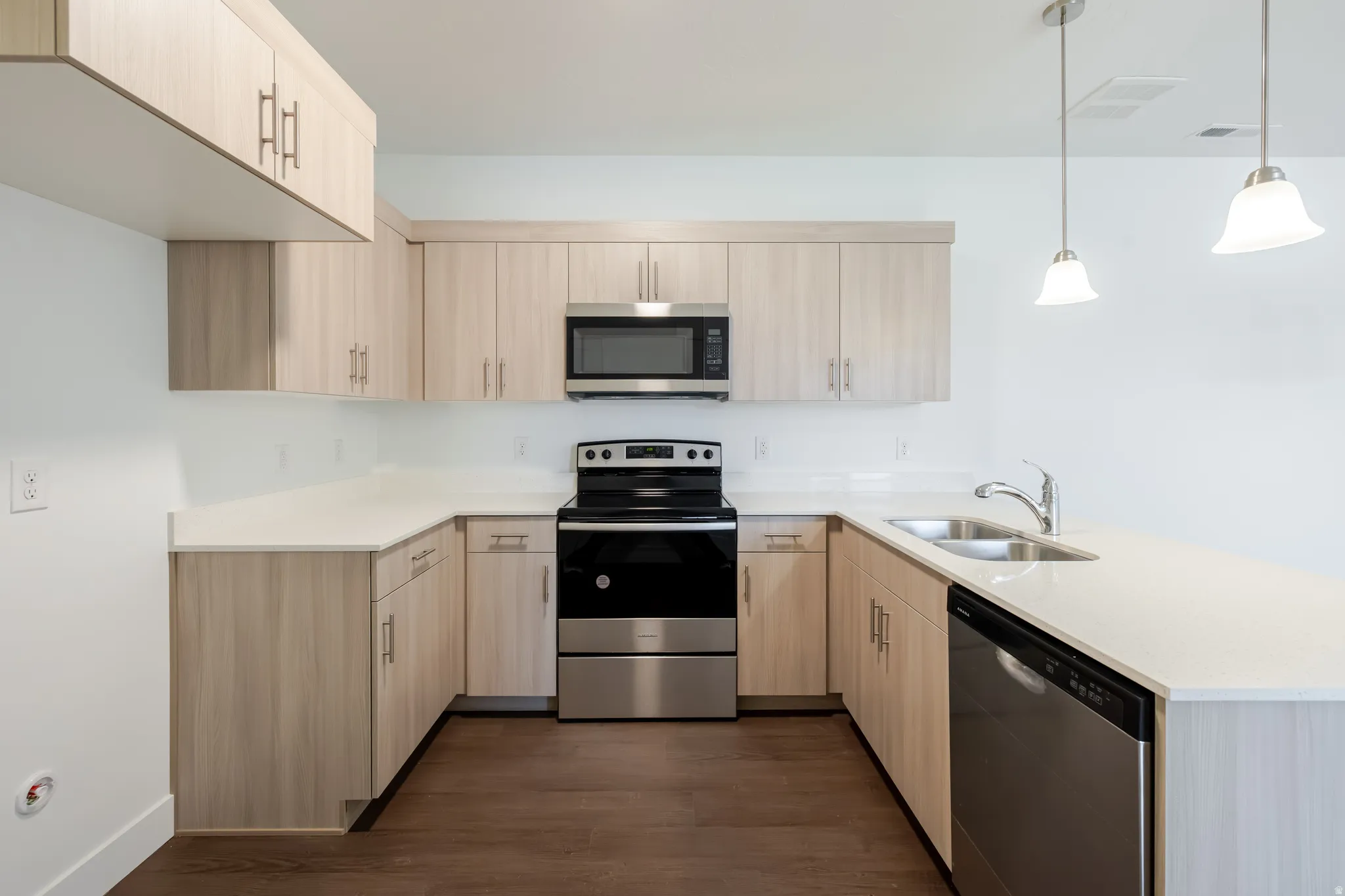 U-shaped kitchen featuring light wood-finish cabinetry, light-toned countertops, stainless steel appliances, and pendant lighting