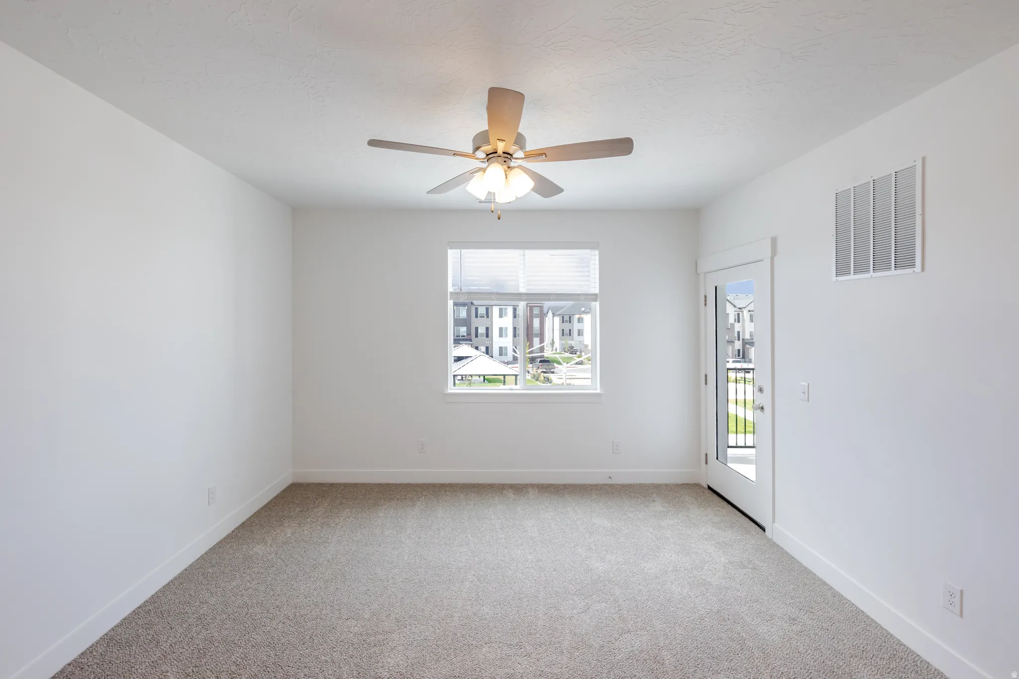 Neutral tone-on-tone carpeting, window with blinds, ceiling fan with integrated lighting, glass-paneled door, and white walls
