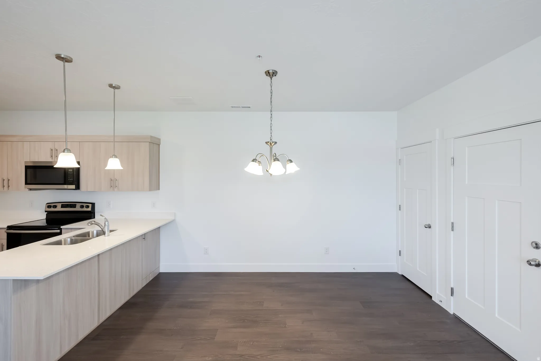 Kitchen with a peninsula featuring light wood-finish cabinetry, built-in microwave, and stainless steel sink