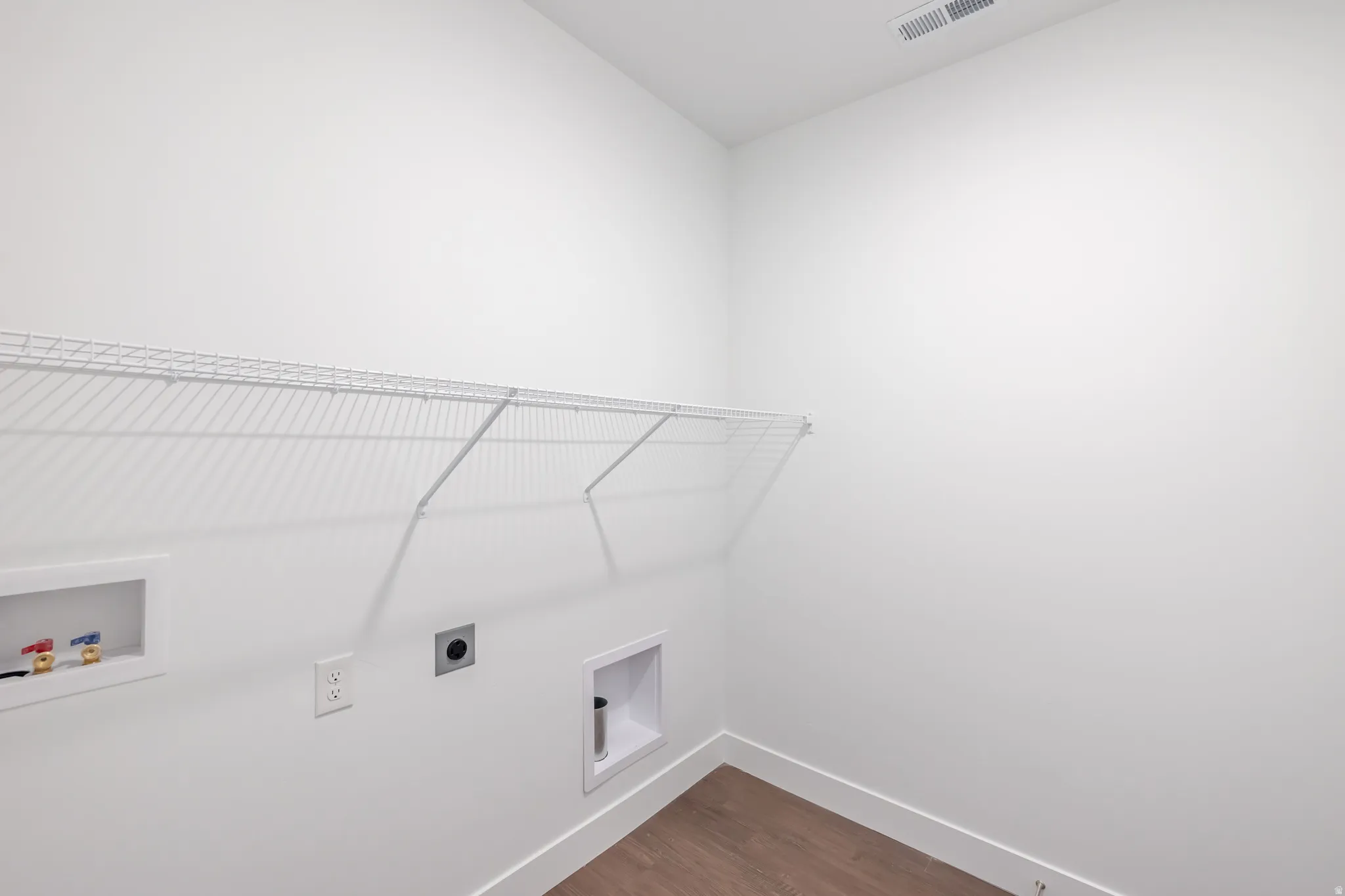 Dedicated laundry space with wire shelving, utility hookups, and wood-finish flooring