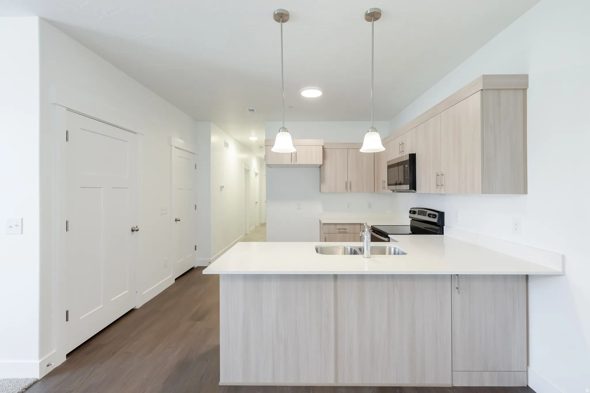 Kitchen featuring light wood-finish cabinetry, stainless steel sink, black appliances, white countertops, and pendant lighting