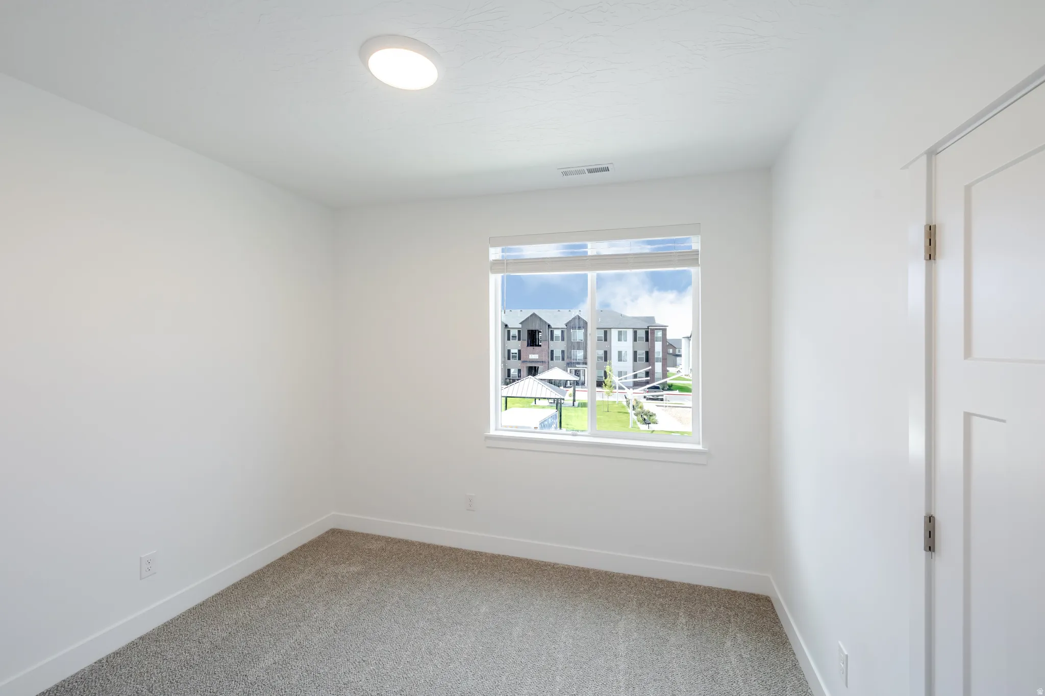 Recessed ceiling light fixture, white interior door, window with white trim, and gray carpet flooring