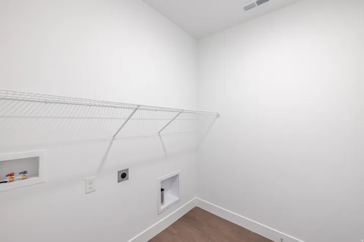 Dedicated laundry space with wire shelving, utility hookups, and wood-finish flooring