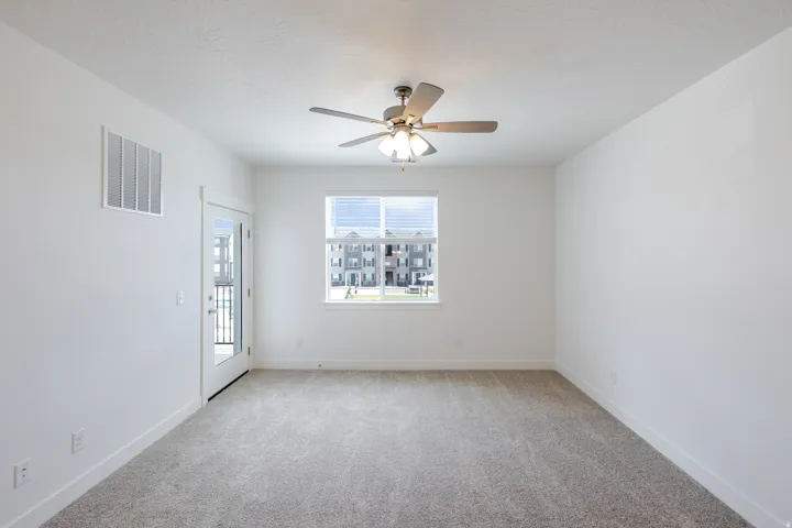Neutral wall finishes, textured carpeting, contemporary ceiling fan, double-pane window, and a glass-paneled door