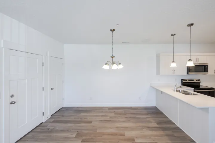 Open-concept living area with wood-finish flooring, white cabinetry, integrated stainless steel appliances, and pendant lighting