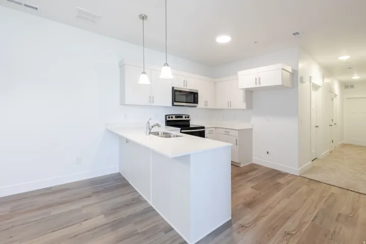 White cabinetry, stainless steel microwave, black range, wood-finish flooring, and pendant lighting