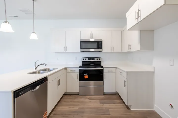 Kitchen featuring white cabinetry, stainless steel appliances, light-toned countertops, a double basin sink with a chrome faucet, and wood-finish flooring