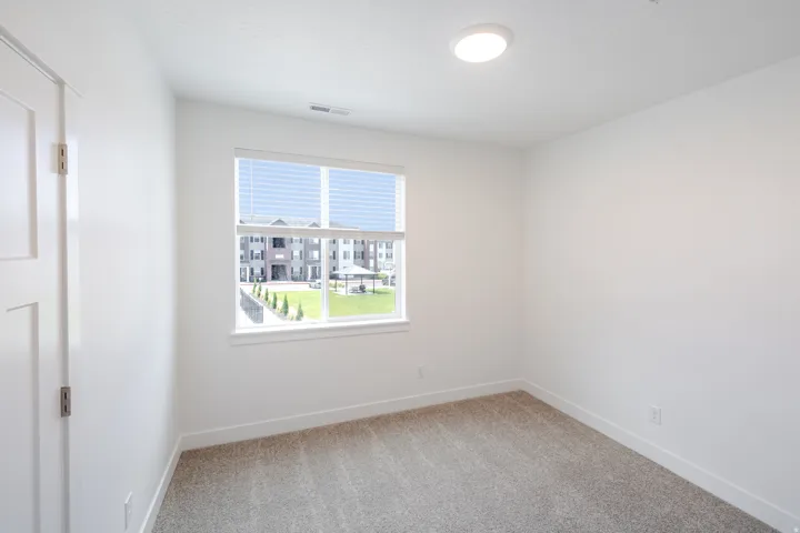 Neutral white wall paint, flush-mount ceiling light, window with horizontal blinds, gray carpet flooring, and white trim