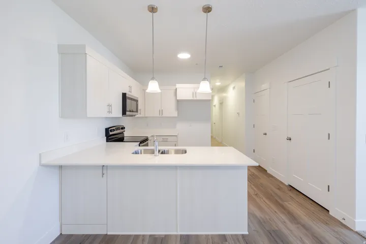 Modern kitchen featuring stainless steel appliances, white cabinetry, a kitchen island with sink, pendant lighting, and wood-finish flooring