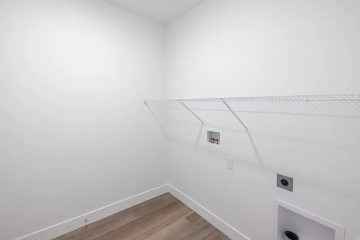 Wood-finish flooring with white trim, white walls, and a white wire shelf