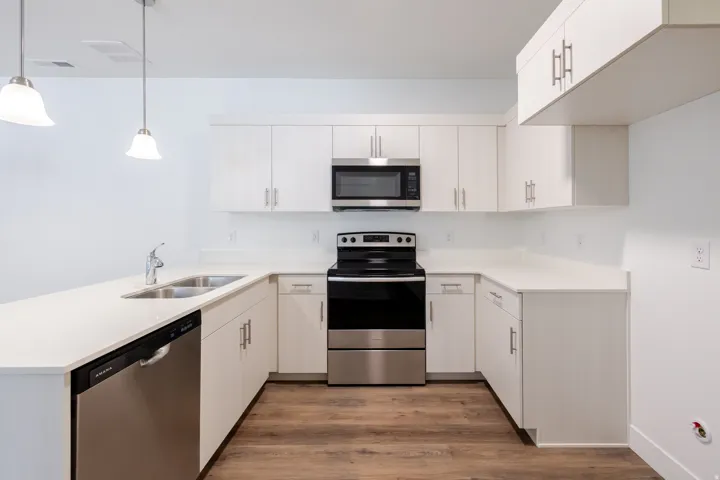 U-shaped kitchen with white cabinetry, stainless steel appliances, white countertops, and wood-finish flooring