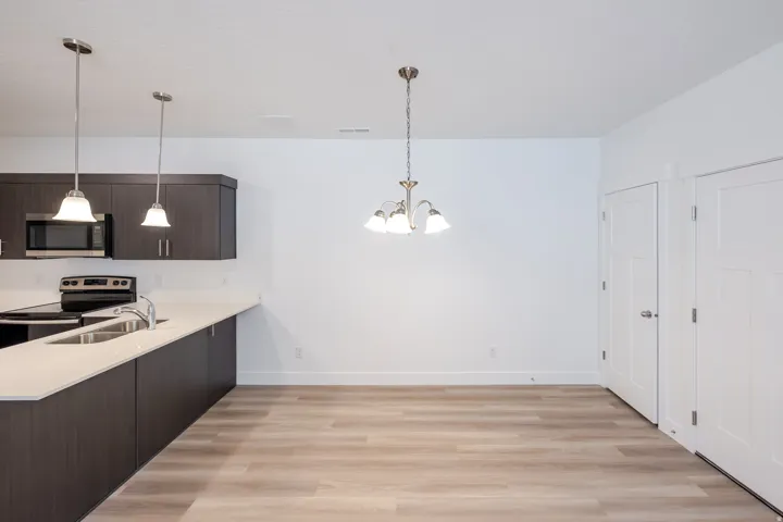 Open-concept kitchen and dining area featuring dark wood-finish cabinetry, light countertops, stainless steel appliances, and wood-finish flooring