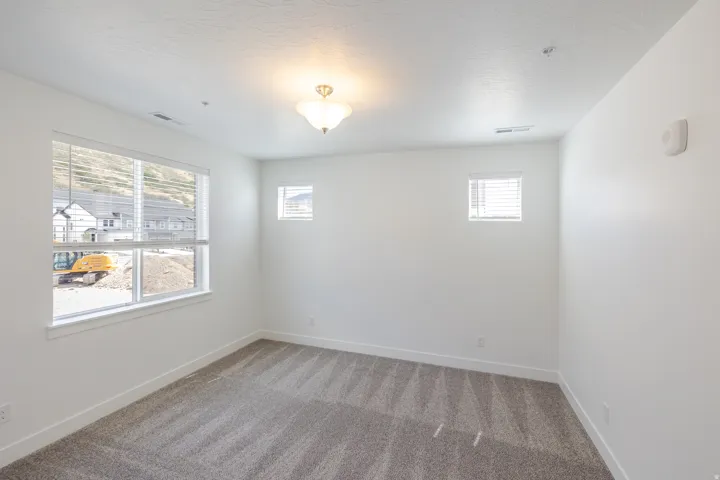 Bright interior with white walls, three windows with blinds, a ceiling-mounted light fixture, and patterned carpet flooring