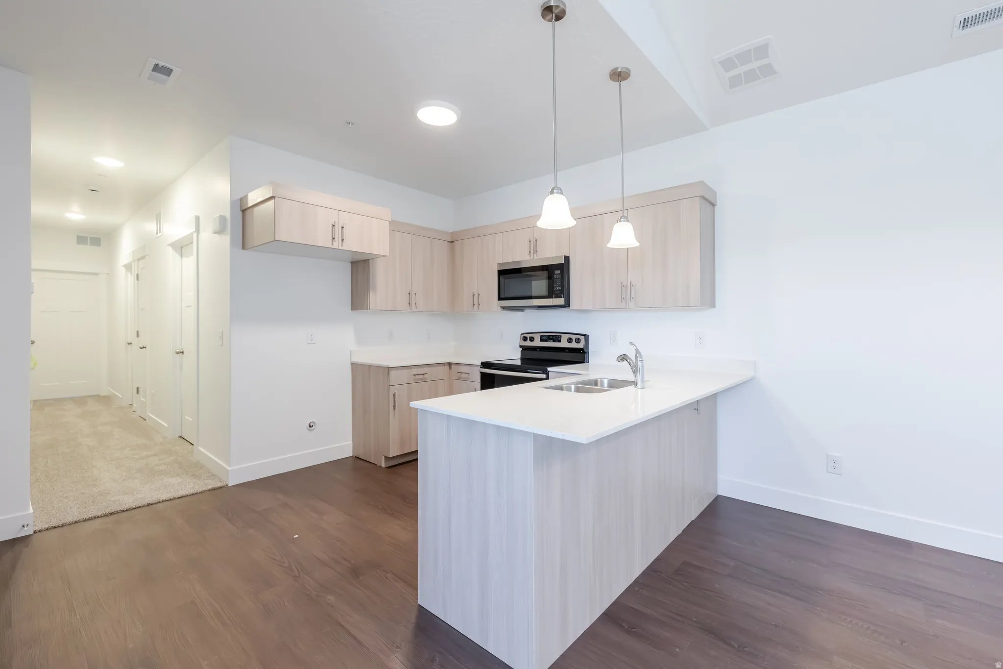 Kitchen featuring light wood-finish cabinetry, white countertops, stainless steel appliances, and a breakfast bar with pendant lighting