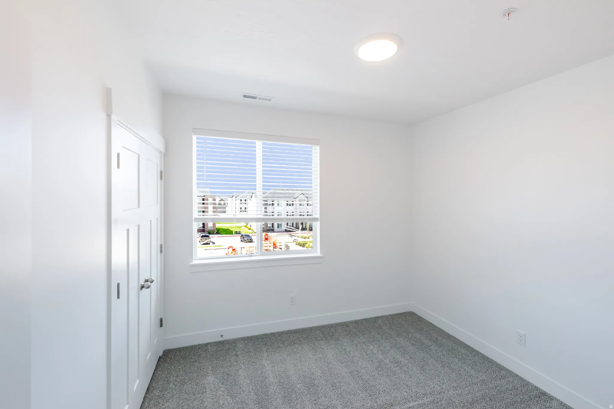 Bright room featuring a window with horizontal blinds, neutral wall paint, gray carpet, and a flush-mount ceiling light