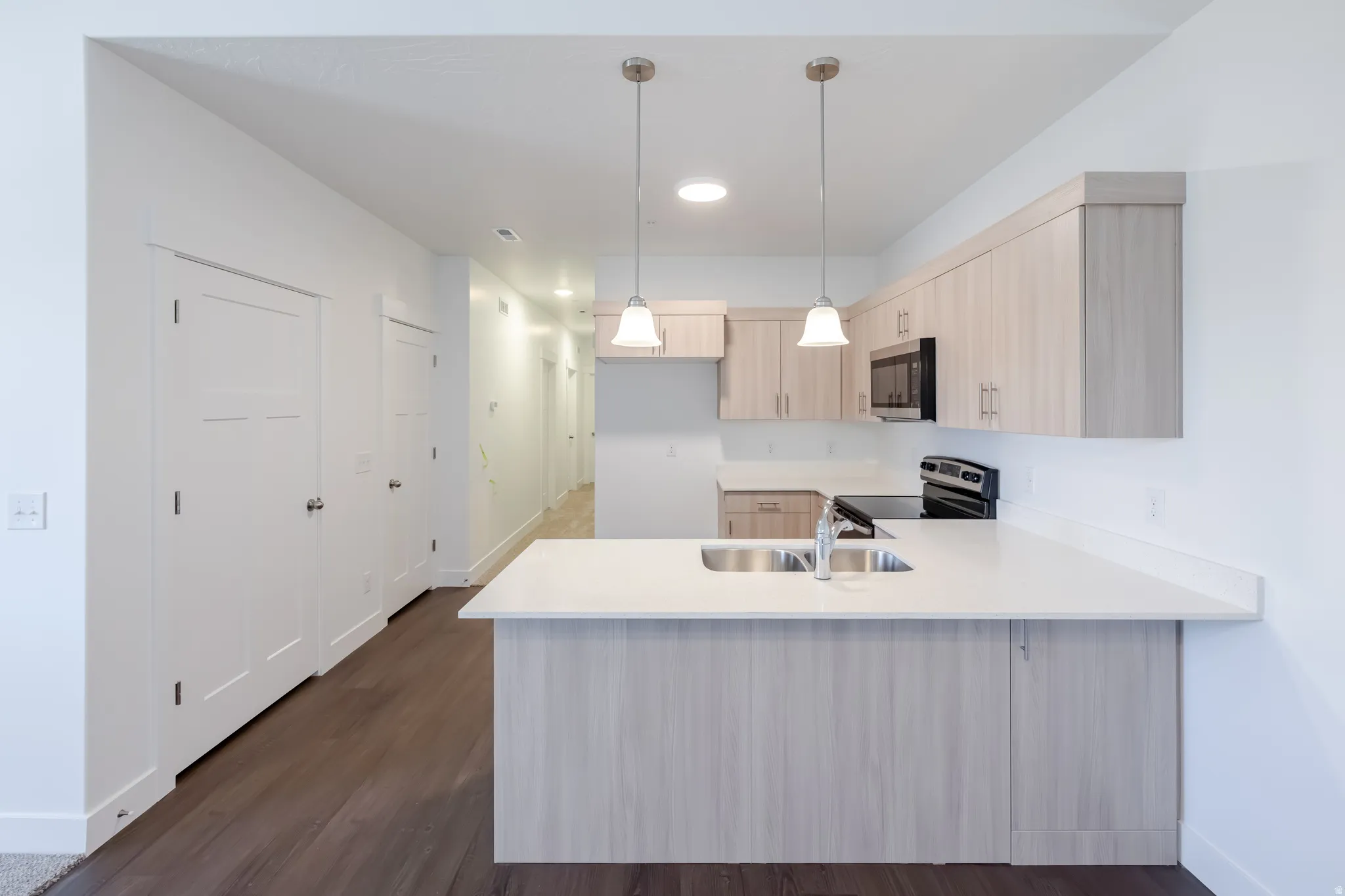 Kitchen with light wood-finish cabinetry, stainless steel sink, black microwave, and black electric range