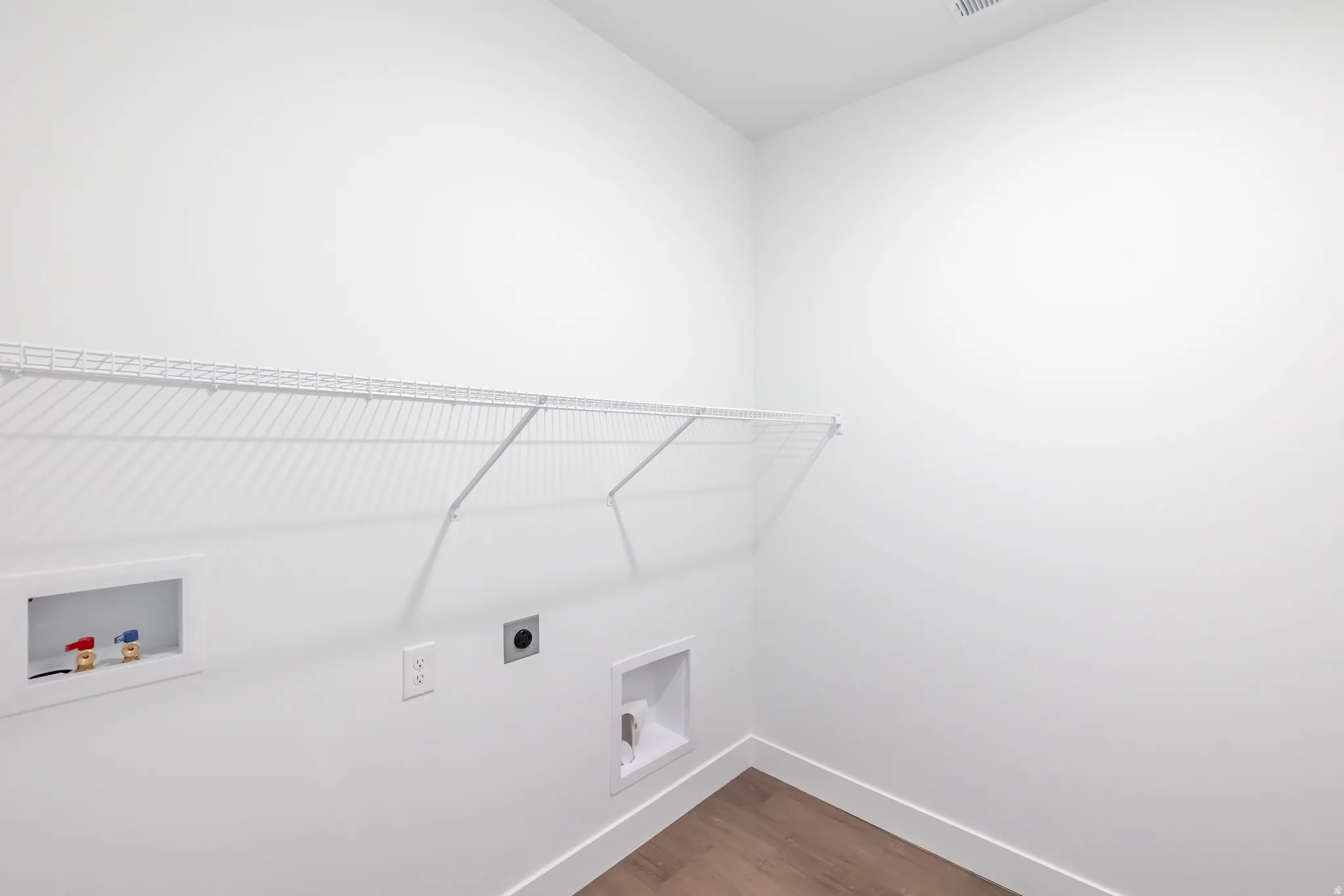 Laundry area featuring wood-finish flooring, white walls, and a wire shelf
