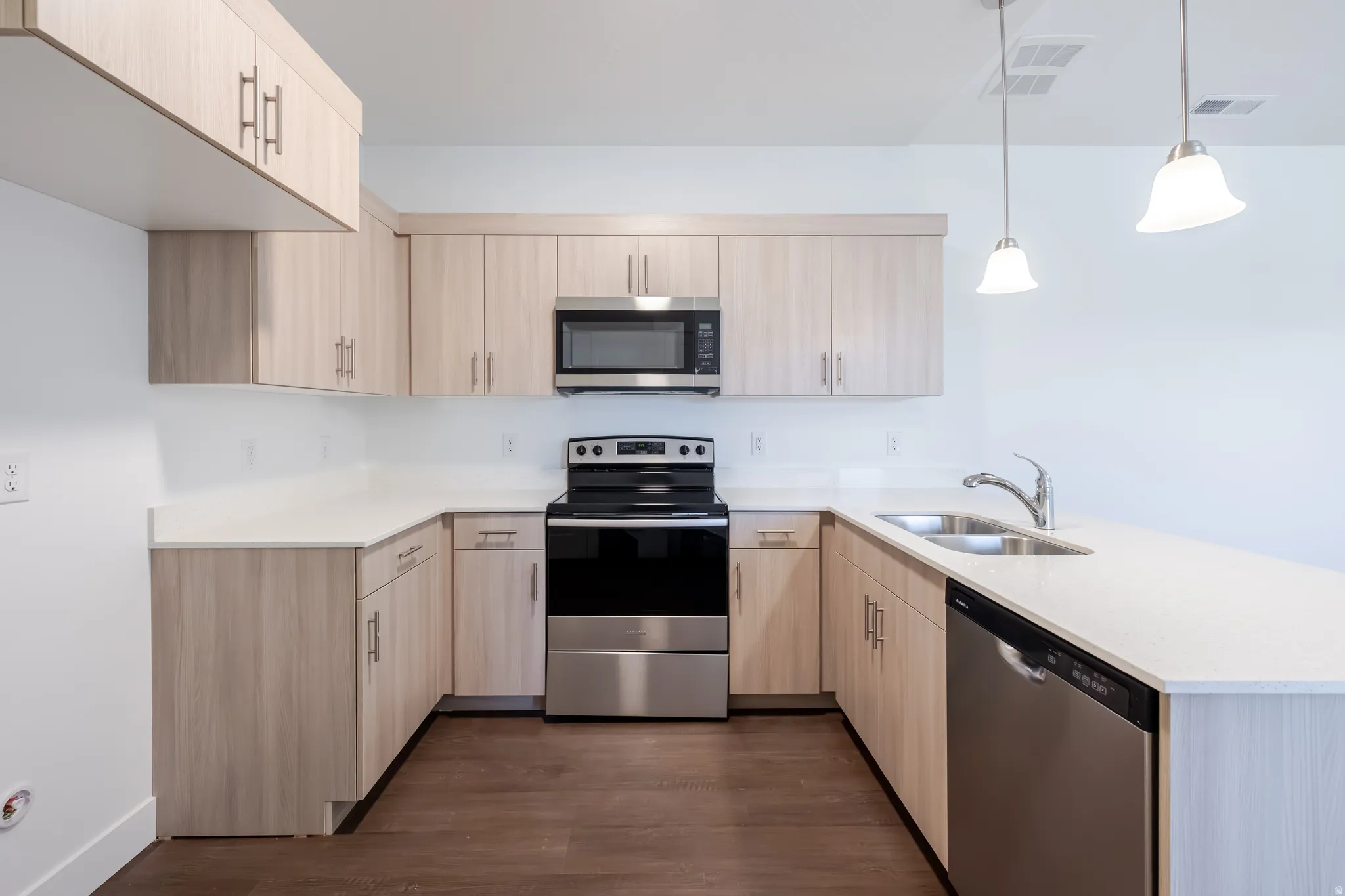Kitchen featuring light wood-finish cabinetry, light-toned countertops, stainless steel appliances, and dark wood-finish flooring