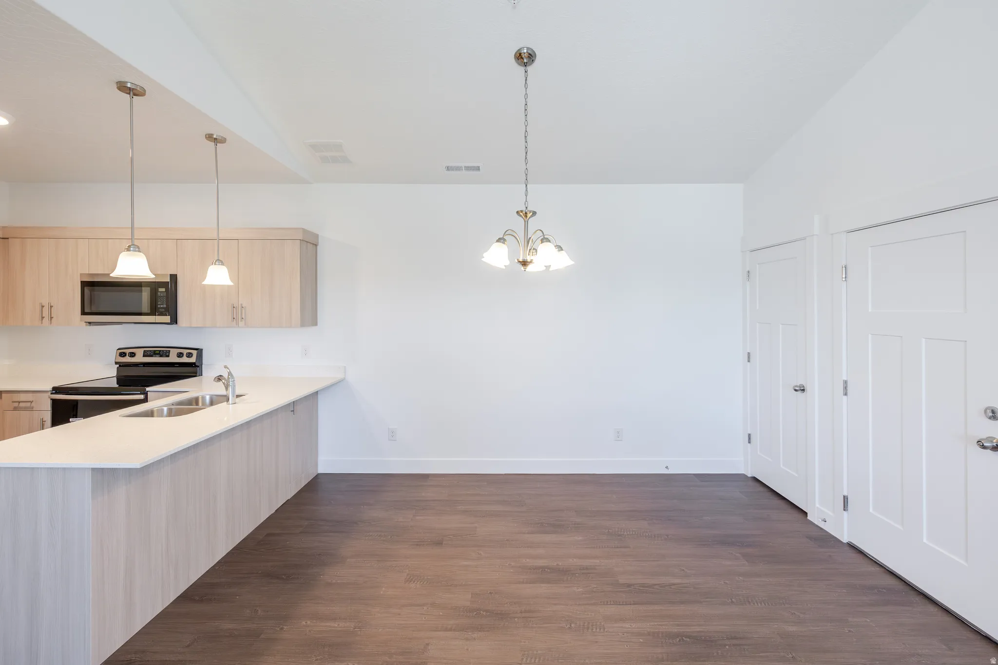 Kitchen featuring light wood-finish cabinetry, stainless steel appliances, a white countertop, and pendant lighting
