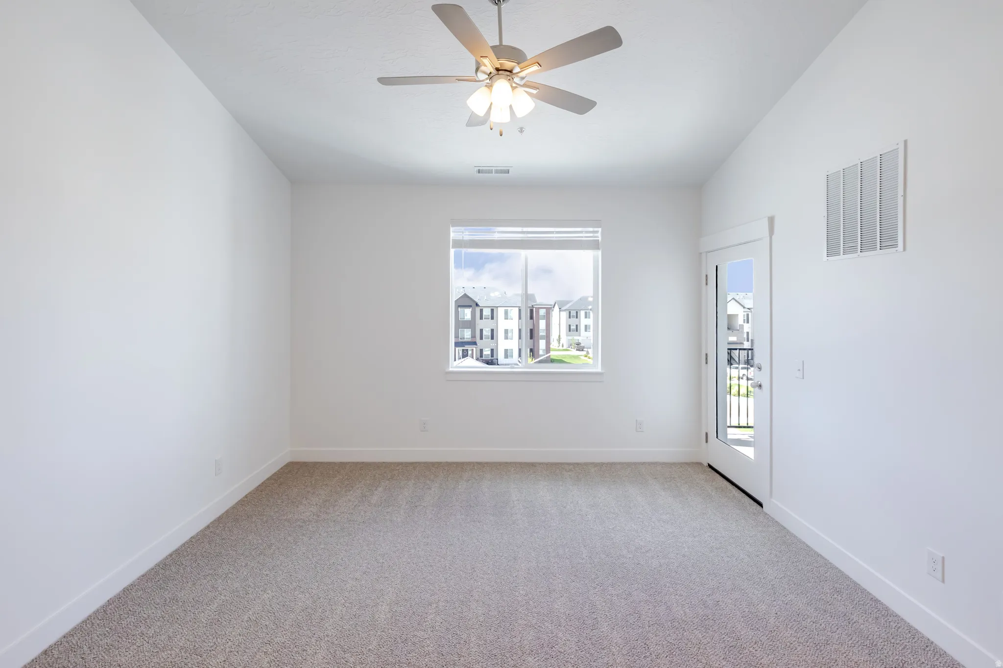 Carpeted room featuring a ceiling fan, white walls, a large window, and a glass-paneled door