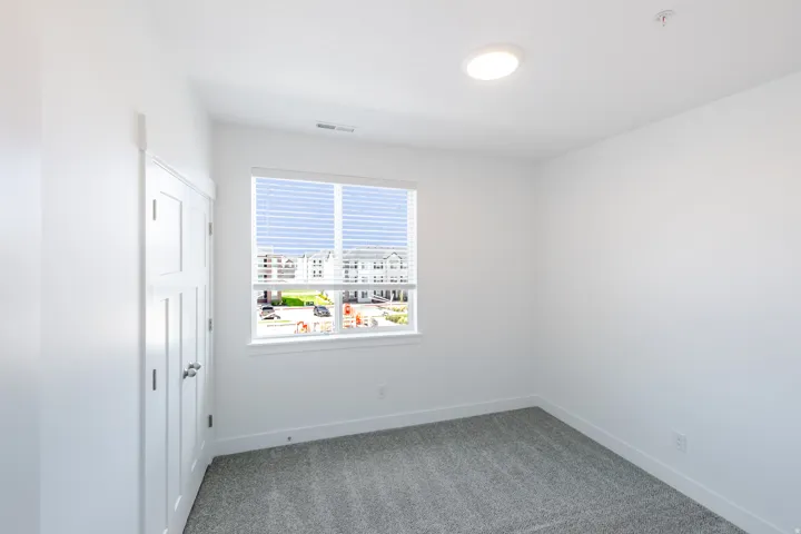 Bright room featuring a window with horizontal blinds, neutral wall paint, gray carpet, and a flush-mount ceiling light