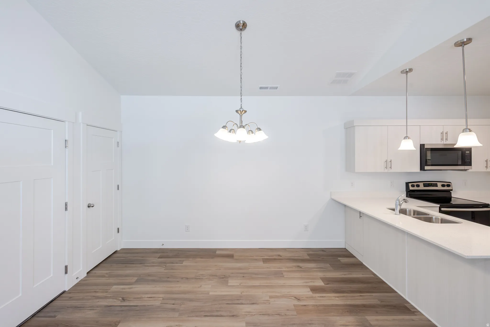 Wood-finish flooring, white cabinetry, integrated stainless-steel microwave, dual basin sink, and pendant lighting