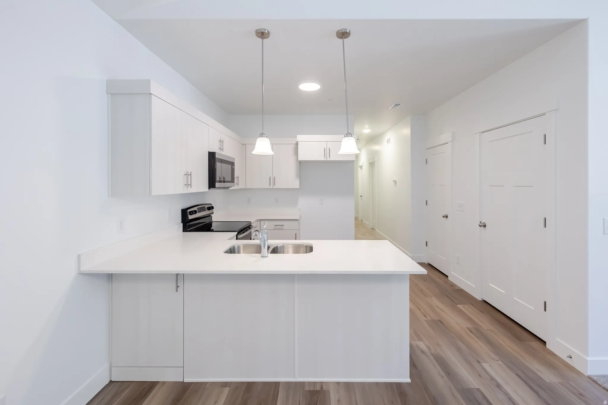 Kitchen featuring a double basin sink, white cabinetry, integrated microwave, and pendant lighting