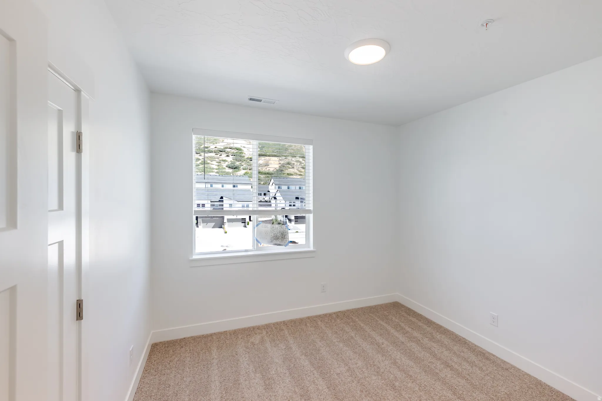 Neutral tone carpet flooring, white painted walls, white trim, window with horizontal blinds, and a flush-mount ceiling light