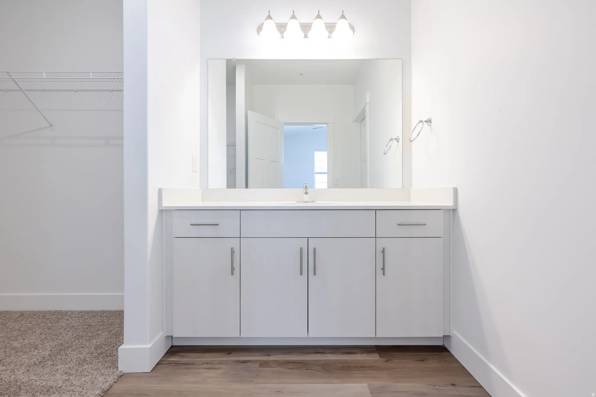 Spa-inspired primary bathroom featuring a custom vanity with ample storage, white quartz countertop, large framed mirror with integrated lighting, and polished chrome hardware and fixtures