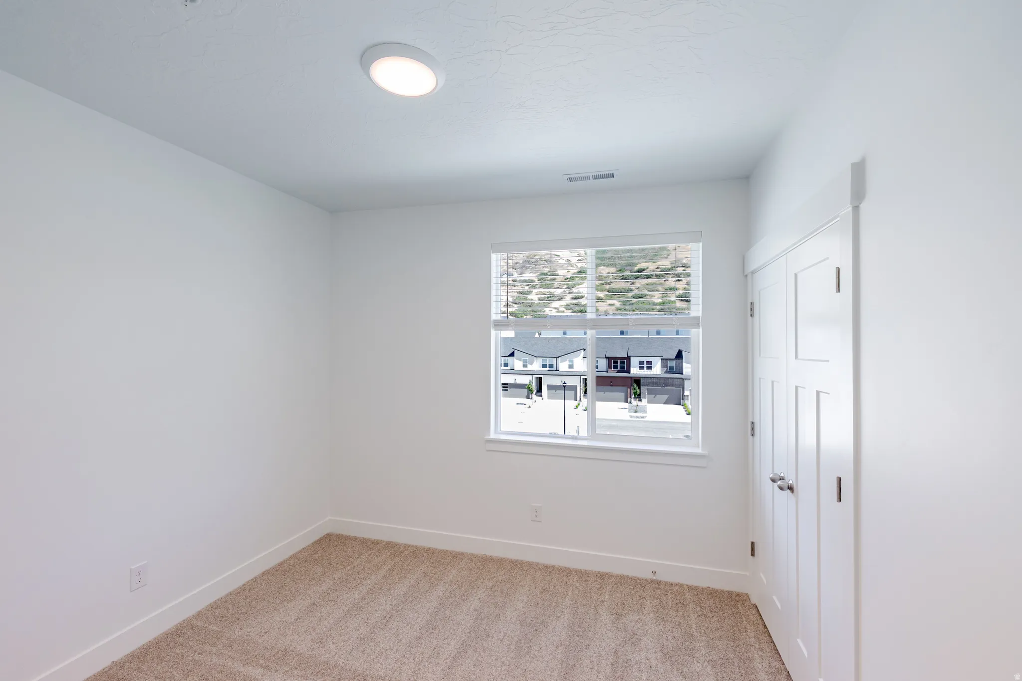 Recessed ceiling light, neutral carpet, white walls, white window trim, white bi-fold closet doors