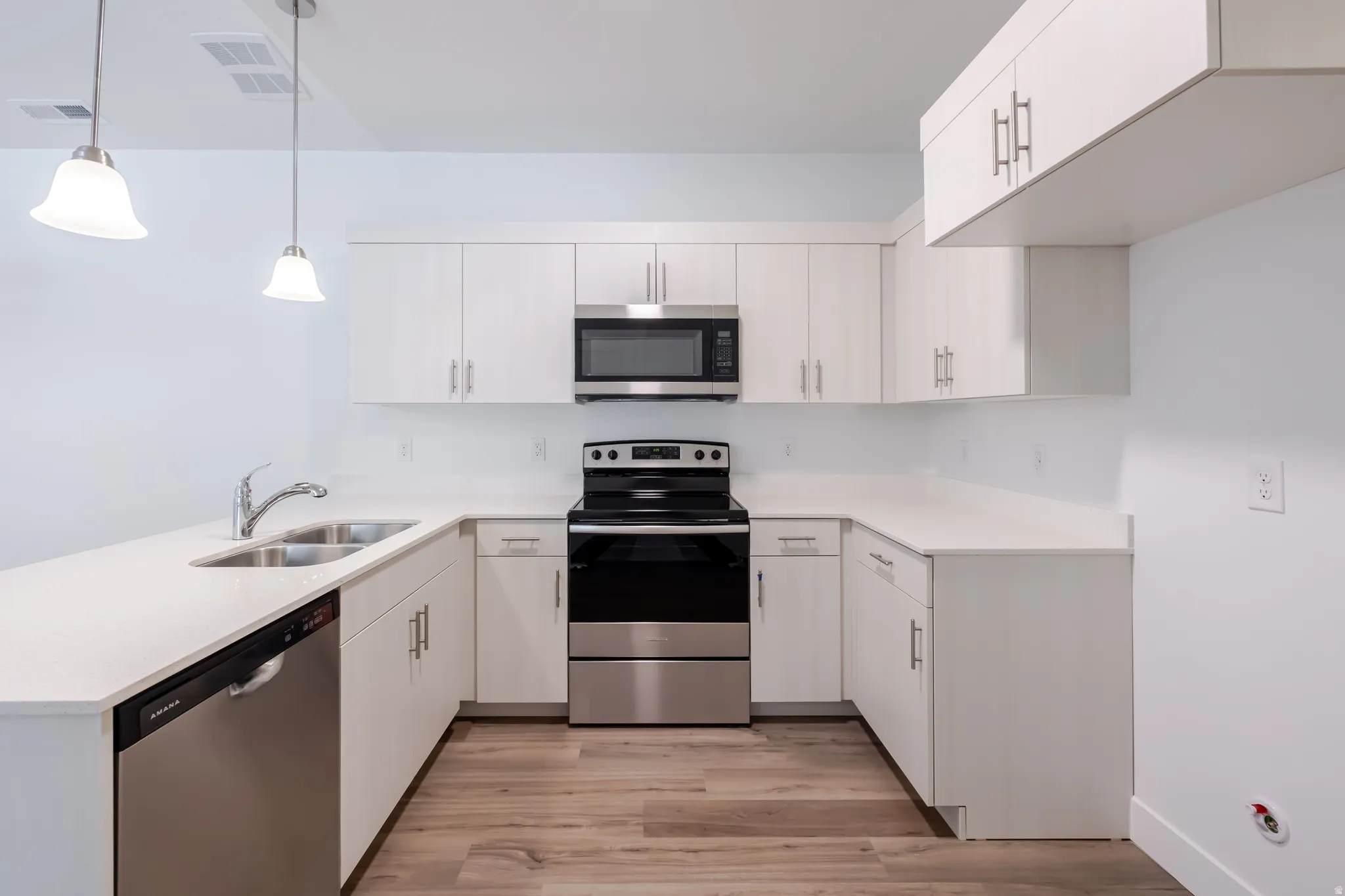 U-shaped kitchen featuring white cabinetry, stainless steel appliances, wood-finish flooring, and pendant lighting