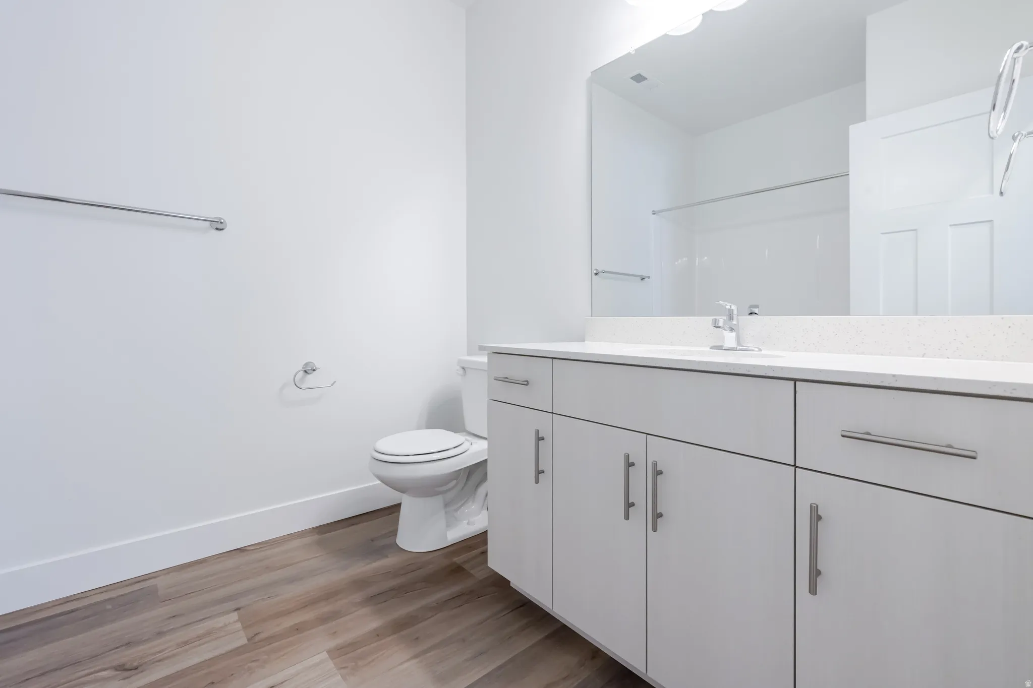 Wood-finish flooring, white vanity with ample storage, integrated basin, and a large wall-mounted mirror