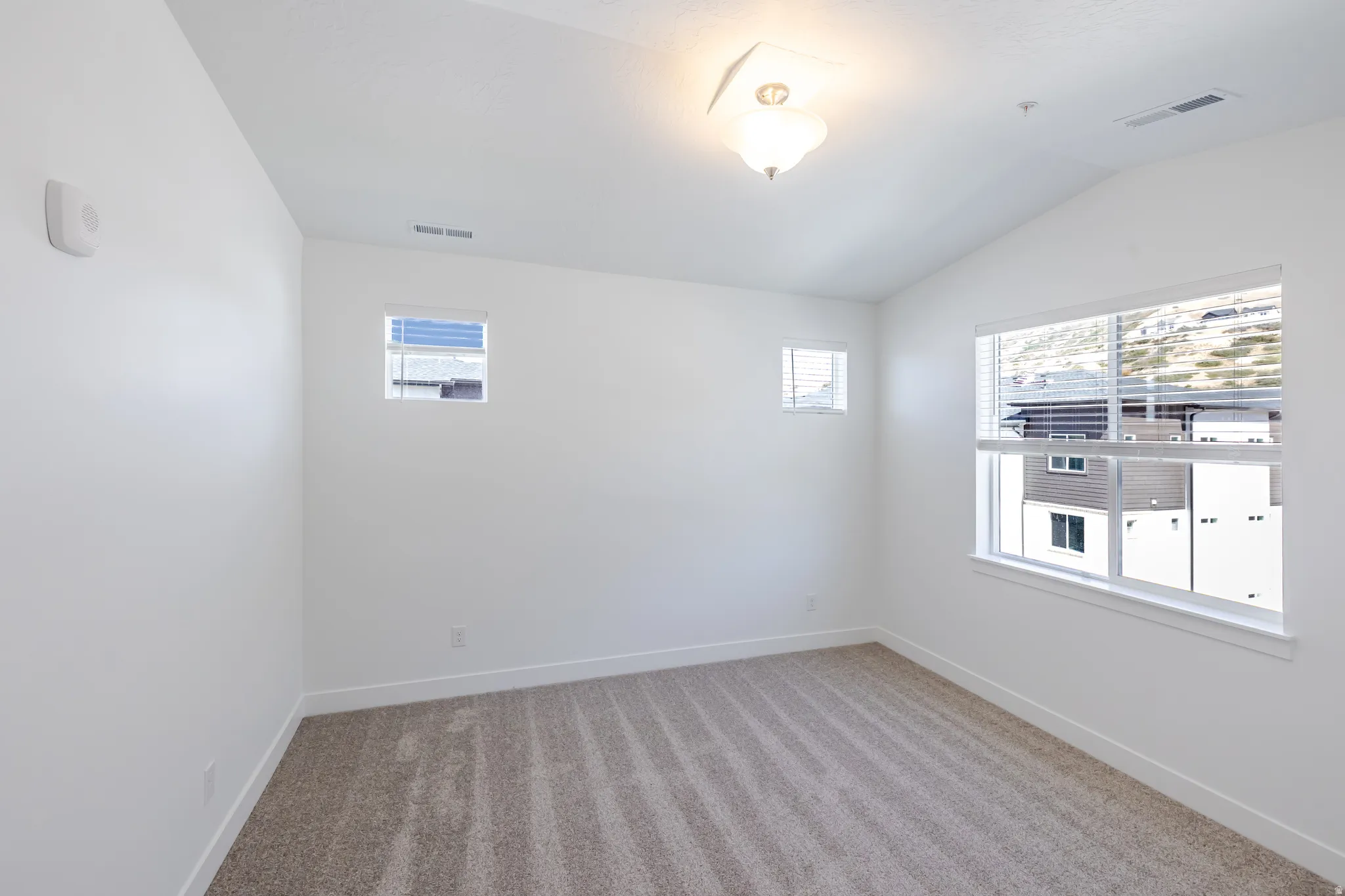 Vaulted ceiling, white walls, large window with blinds, additional smaller windows, and carpeting