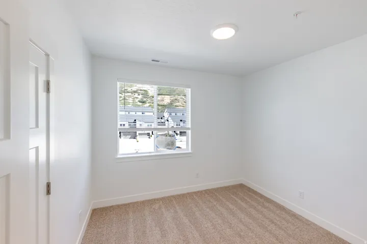 Neutral tone carpet flooring, white painted walls, white trim, window with horizontal blinds, and a flush-mount ceiling light