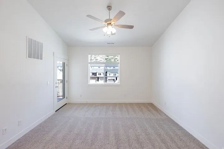 Plush carpet flooring, white walls, and a ceiling fan with integrated lighting