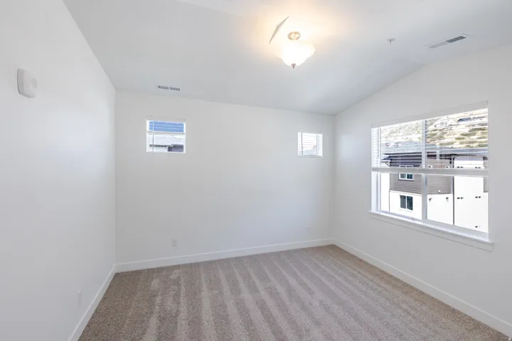 Vaulted ceiling, white walls, large window with blinds, additional smaller windows, and carpeting