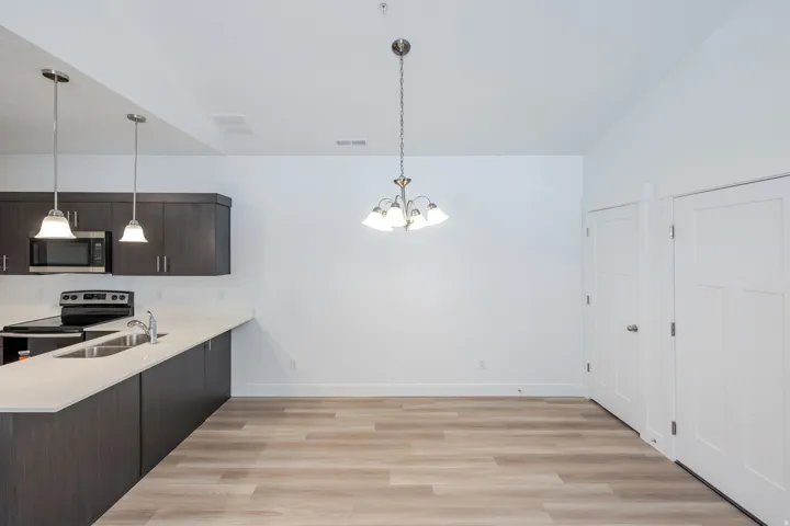Kitchen and dining area featuring wood-finish flooring, dark wood cabinetry, light countertops, stainless steel appliances, and ceiling-mounted light fixtures