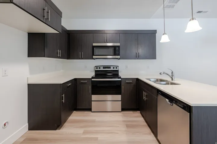 U-shaped kitchen featuring dark wood-finish cabinetry, light-toned countertops, stainless steel appliances, and wood-finish flooring