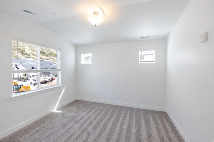 White wall finishes, textured carpet flooring, single flush mount light fixture, multiple windows with blinds