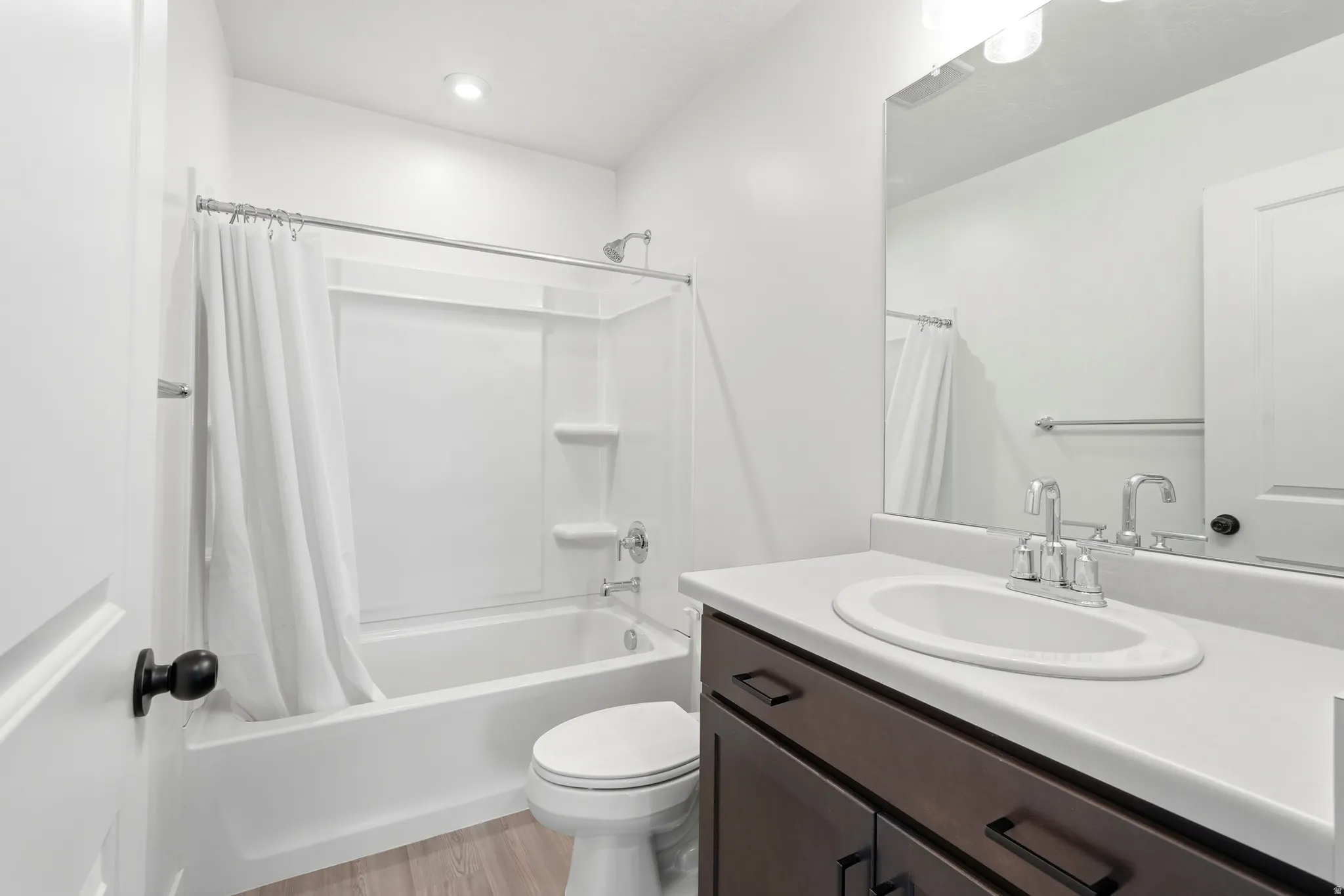 Bathroom featuring a white tub/shower combination, dark wood-finish vanity with a light-colored countertop, and a large wall-mounted mirror