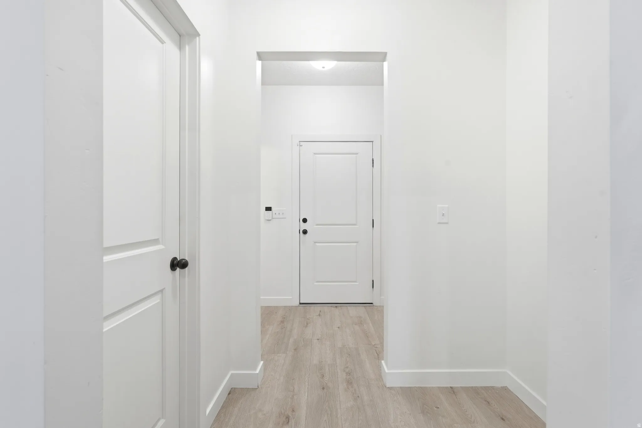 Hallway with light wood-finish flooring, white baseboards, and white walls