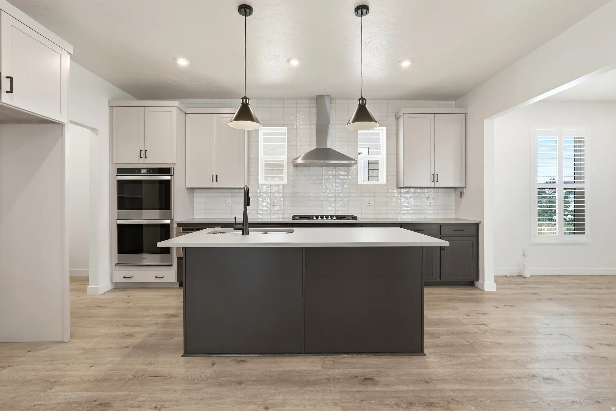 Contemporary kitchen featuring a large central island with a sink, light wood-finish flooring, white upper cabinetry, dark lower cabinetry, and a subway tile backsplash