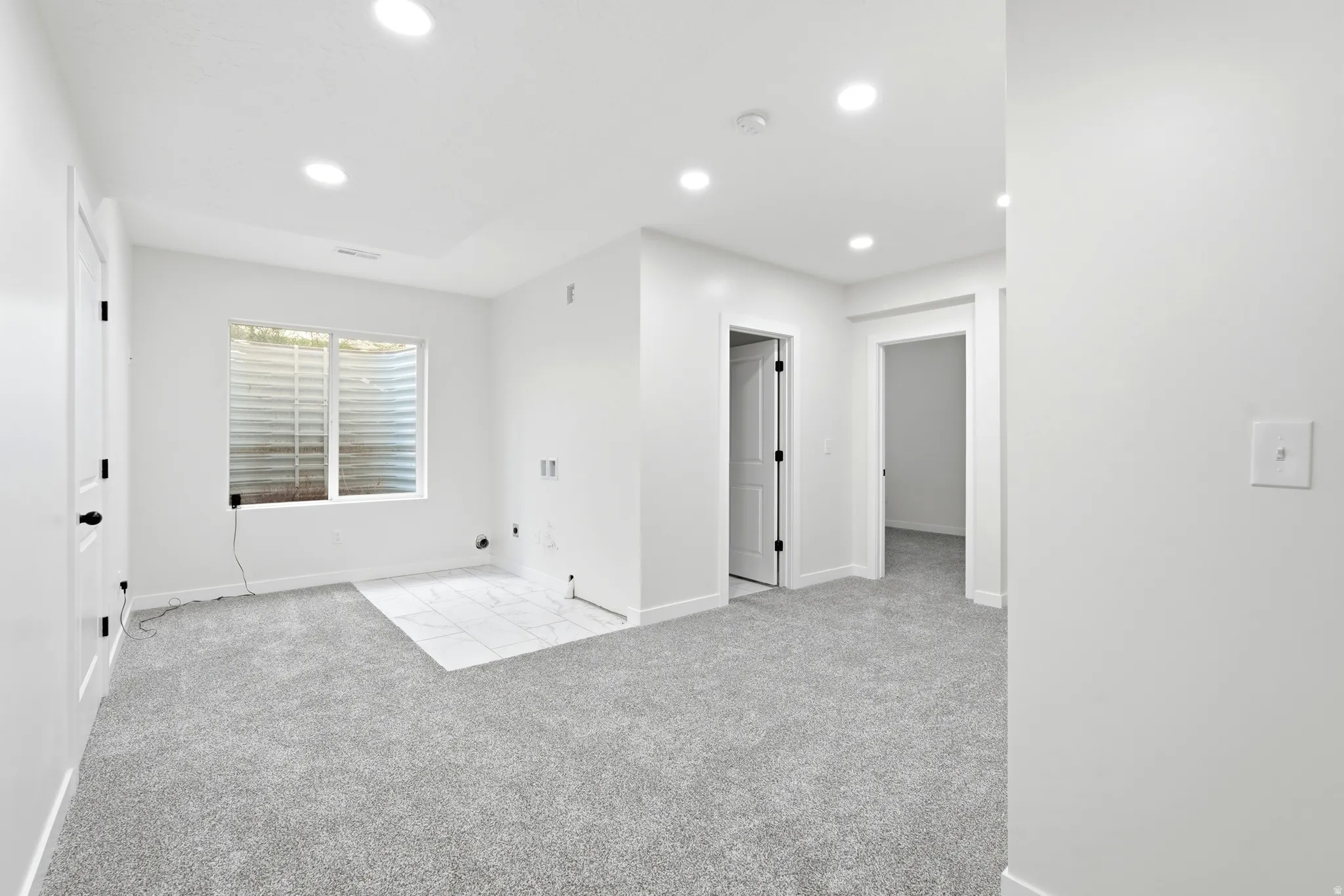 Spacious interior featuring light gray carpeting, a window with horizontal blinds, and recessed lighting